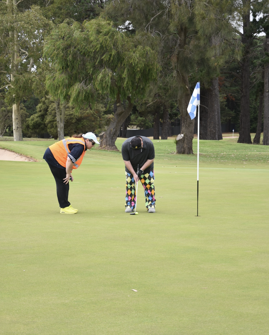 Golfer lining up on the green ready to putt while the Caddie is standing behind giving instructions